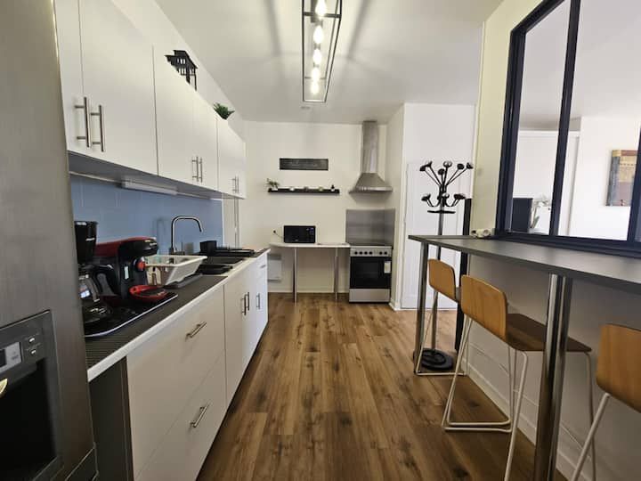 Cuisine moderne blanche avec parquet, électroménager noir et bar avec tabourets.