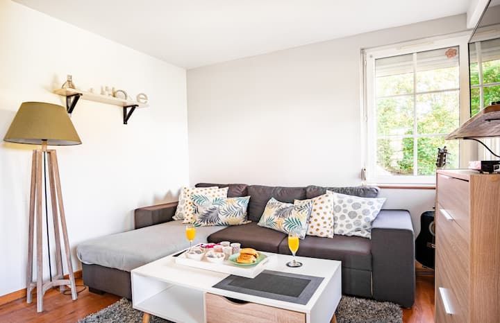 Salon avec canapé gris, table basse blanche, lampe en bois et fenêtre laissant entrer la lumière naturelle.