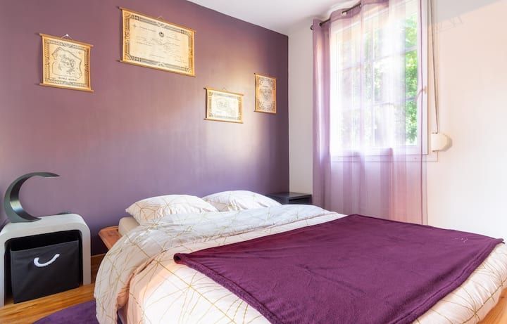 Chambre avec un mur d'accent violet, un lit, des tableaux encadrés et des rideaux transparents.
