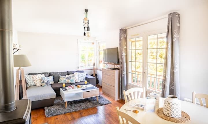 Salon confortable avec canapé d'angle gris, télévision et portes-fenêtres donnant sur un balcon.