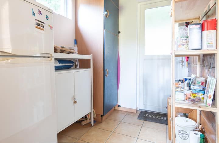 Petite buanderie avec réfrigérateur, armoire et étagères ouvertes remplies de fournitures.