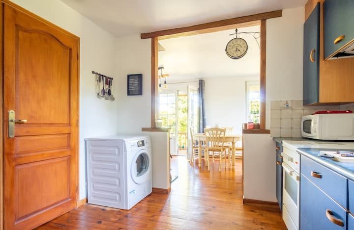 Cuisine avec porte en bois, lave-linge et vue sur la salle à manger avec table et chaises.