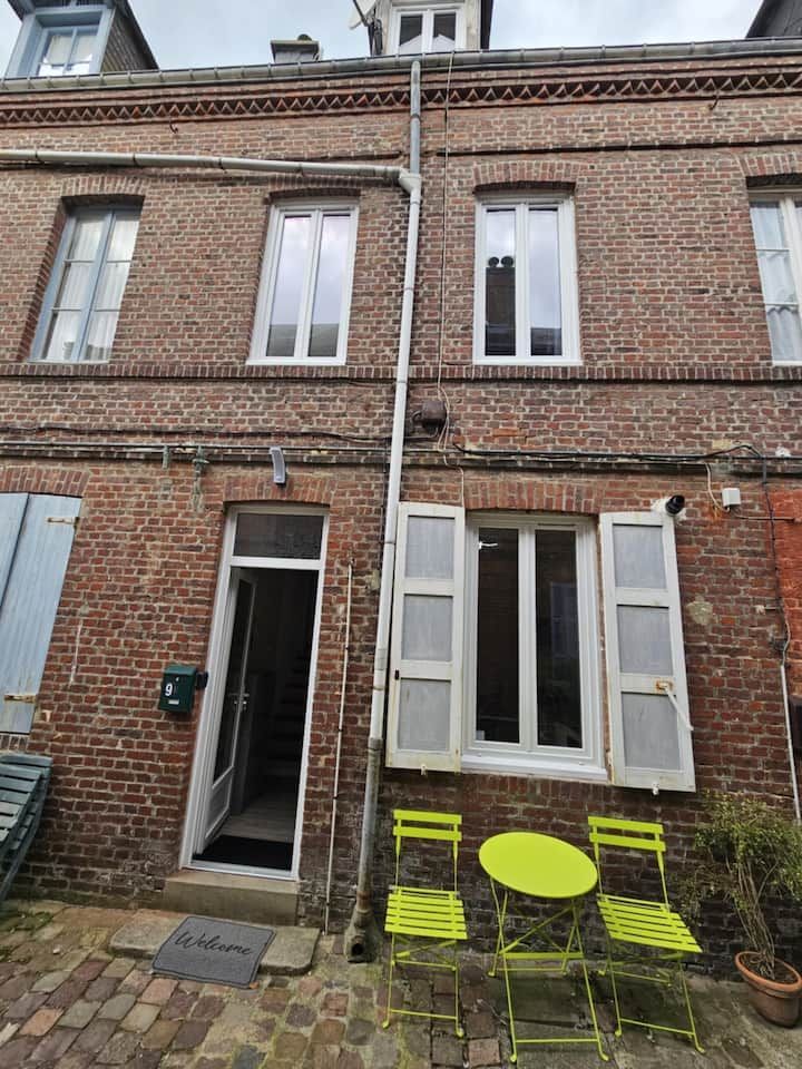 Façade de maison de ville en briques avec volets blancs ouverts, porte noire et marquages jaune fluo du patio sous la fenêtre