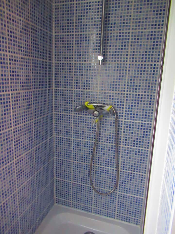 Douche avec murs carrelés bleus, robinetterie chromée et receveur de douche blanc.