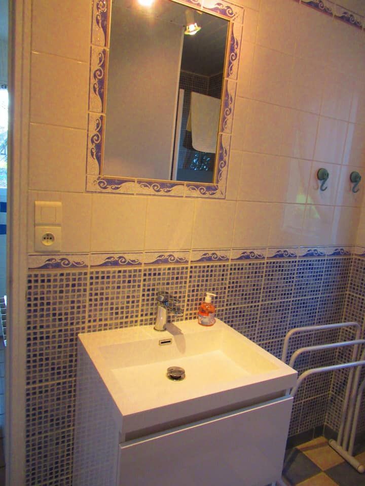 Salle de bains avec lavabo blanc, carrelage en mosaïque bleue, miroir et porte-serviettes.