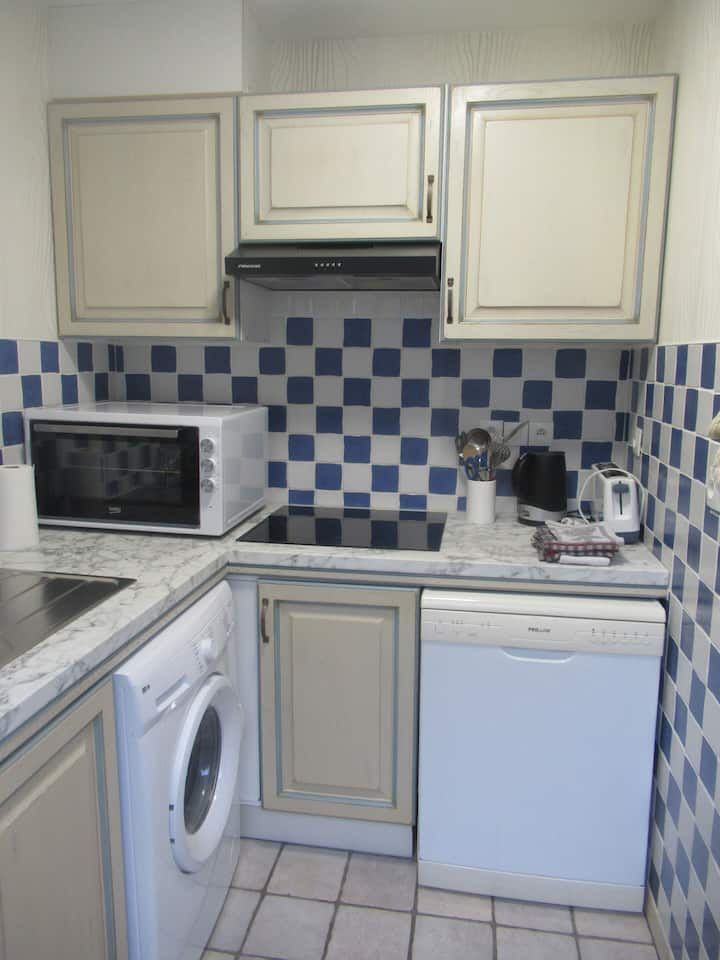 Petite cuisine avec appareils électroménagers blancs, placards gris clair, crédence à carreaux bleus et micro-ondes.