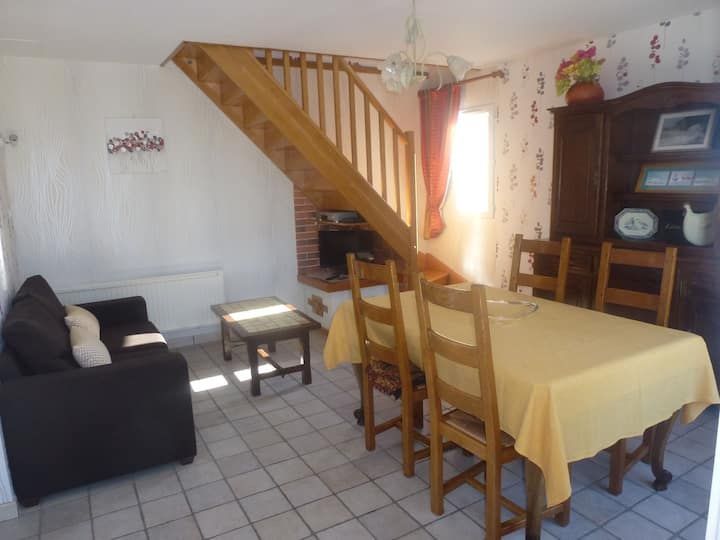 Salle à manger avec table, chaises, canapé, escalier et armoire. Belle lumière naturelle grâce à la fenêtre.