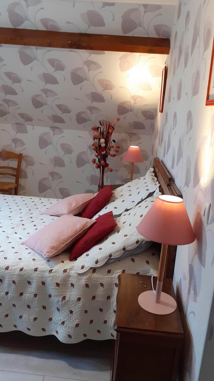 Chambre avec lit, oreillers, lampes, papier peint à motifs floraux et poutre en bois.