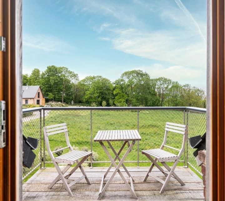 Une table de patio blanche et deux chaises sur une terrasse en bois donnant sur un jardin verdoyant et des arbres