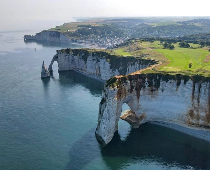 Des falaises de craie blanche s'élèvent au-dessus d'une mer bleue calme, surmontées d'un plateau herbeux verdoyant.