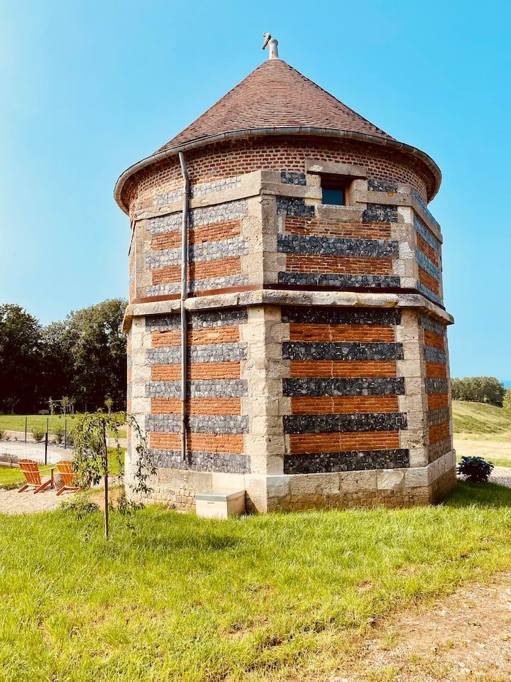 Tour ronde en pierre avec des bandes de briques rayées et un toit conique dans un champ herbeux sous un ciel bleu