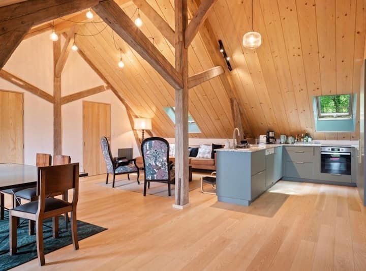 Appartement de type loft avec plafond lambrissé, poutres apparentes, cuisine et coin repas.