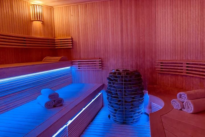 Sauna éclairé à la lumière bleue avec bancs en bois, pierres empilées et serviettes roulées