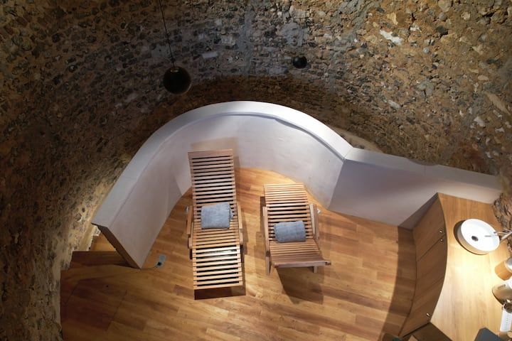 Vue aérienne d'un salon incurvé avec deux chaises longues en bois sur un parquet, à côté d'une table d'appoint ronde et d'un mur en briques.
