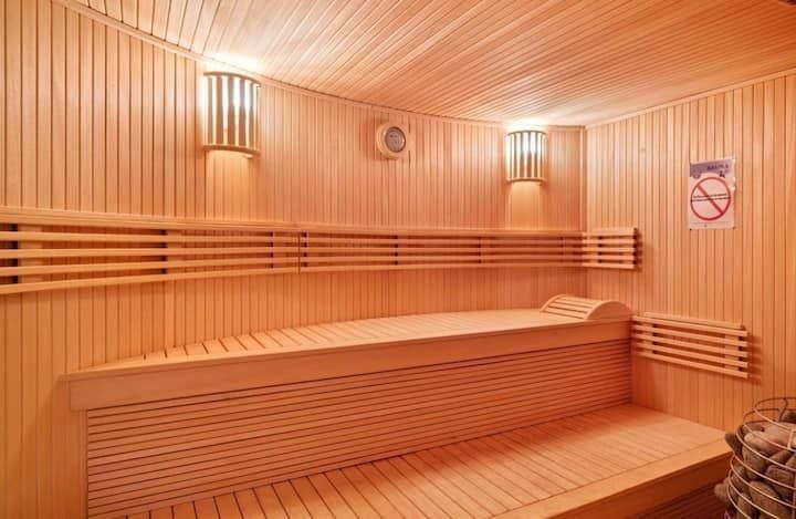 Sauna lambrissé avec banquettes, éclairage chaleureux et panneau « Interdit de fumer » au mur.