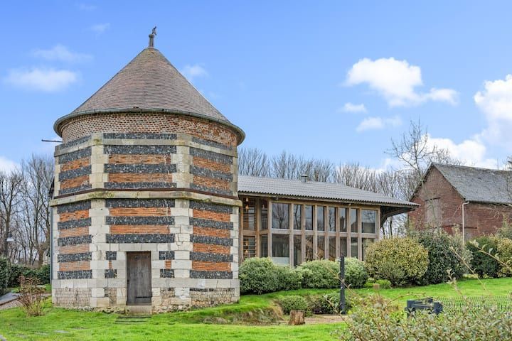 Tour ronde en briques rayées à côté d'un bâtiment moderne en verre dans un parc verdoyant sous un ciel nuageux