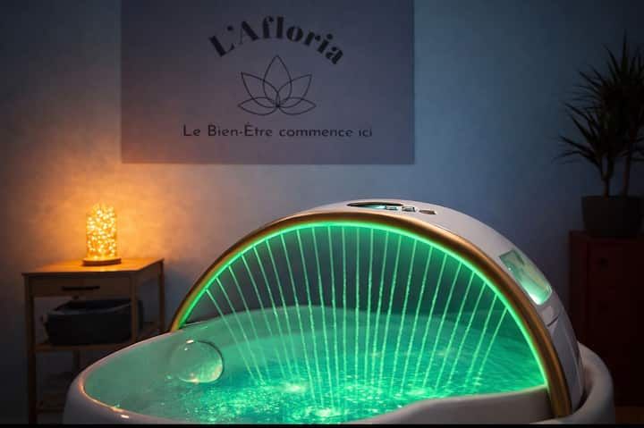 Capsule de spa verte lumineuse dans une pièce tamisée avec une lampe latérale allumée et un logo mural