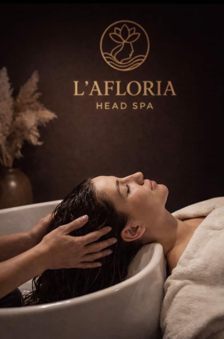 Une femme reçoit un massage du cuir chevelu au spa L'Afloria Head Spa, allongée dans une cabine de spa sombre.