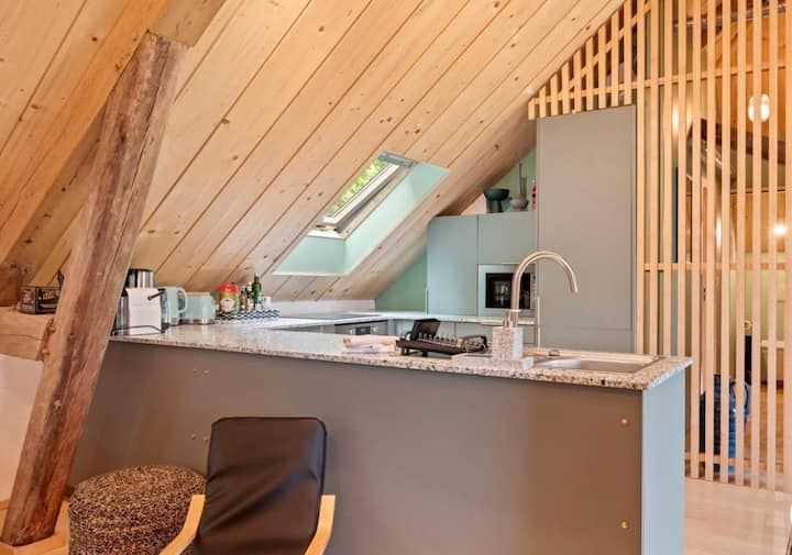 Cuisine de style loft avec plafond en bois incliné, puits de lumière, comptoir en marbre et armoires grises.