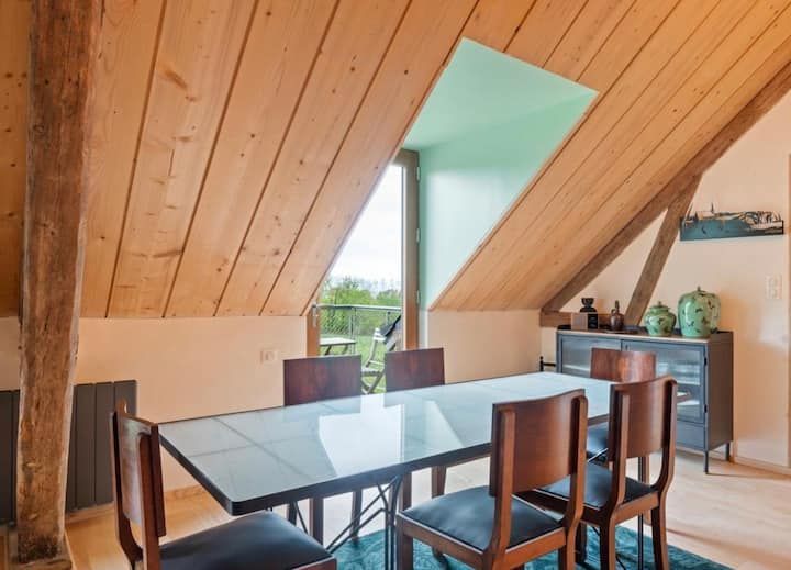 Salle à manger mansardée lambrissée avec table en verre, chaises en bois et fenêtre de style puits de lumière