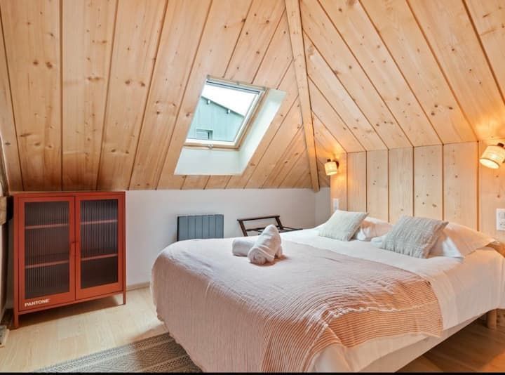 Chambre mansardée confortable avec murs lambrissés, puits de lumière et lit impeccablement fait avec draps blancs
