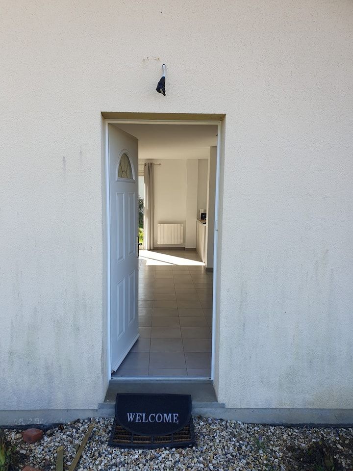 Une porte blanche ouverte avec un paillasson donne sur un couloir intérieur lumineux.