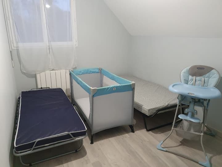 Petite chambre mansardée avec un lit, une table à langer et une chaise haute pour bébé près d'une fenêtre