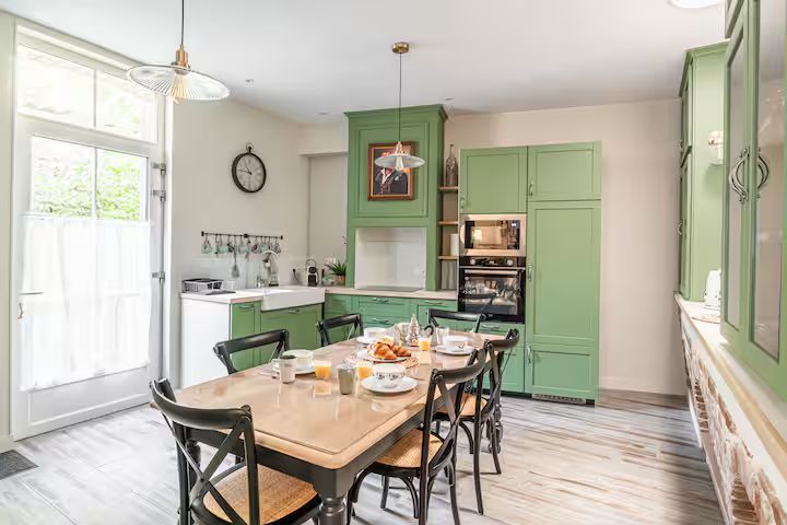 Cuisine avec placards verts, table en bois pour le petit-déjeuner et grande fenêtre.