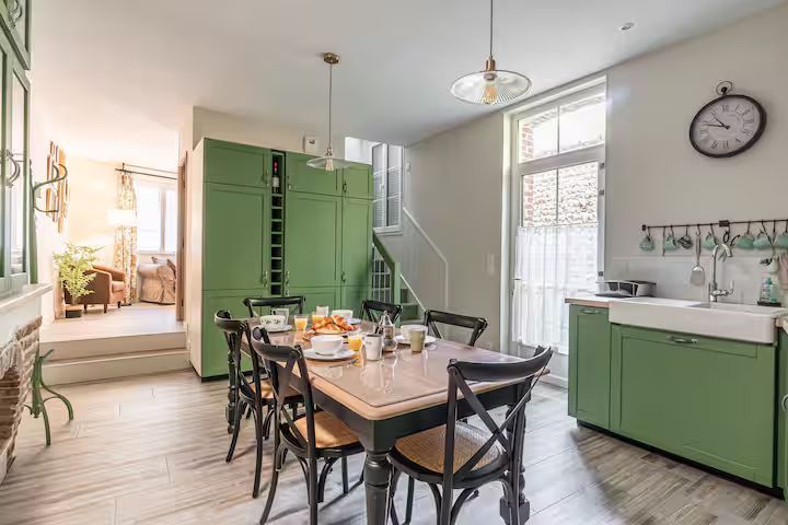 Salle à manger avec placards verts, table dressée pour six personnes, escalier en arrière-plan.