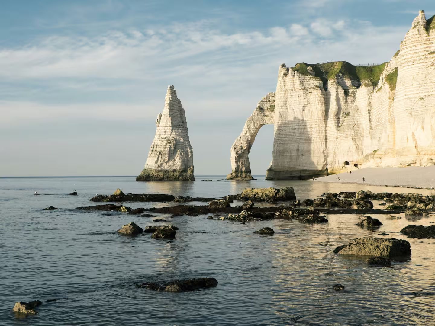 Falaises de craie blanche avec des arches et un rocher isolé sur un rivage rocheux sous un ciel bleu.