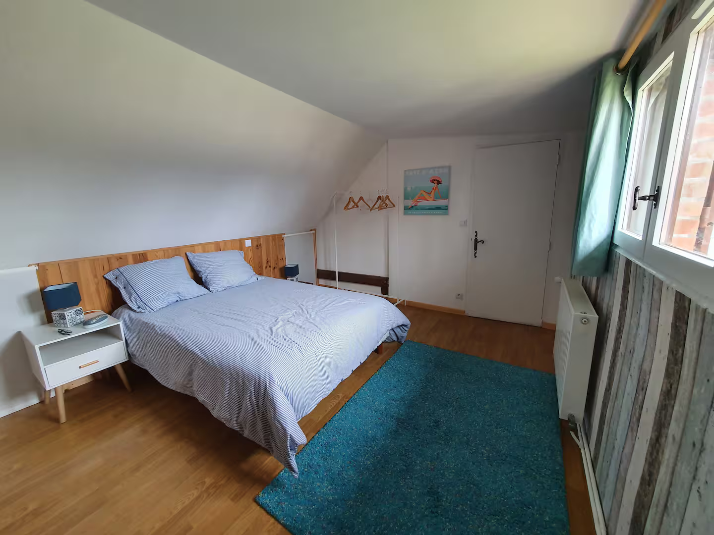 Une chambre avec un lit, une table de chevet, un tapis et une fenêtre.