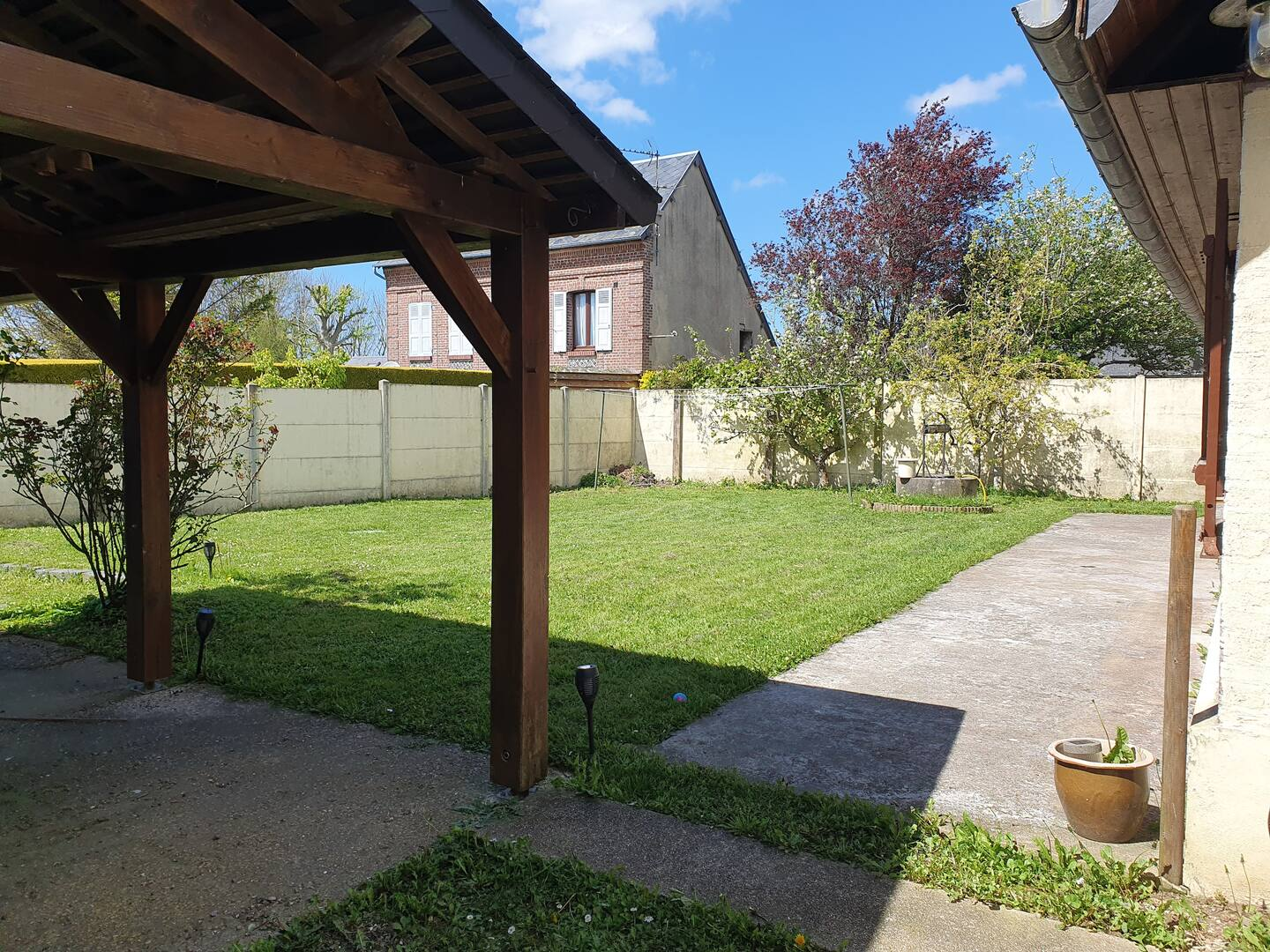 Une grande cour verdoyante avec un espace couvert et une maison en arrière-plan.