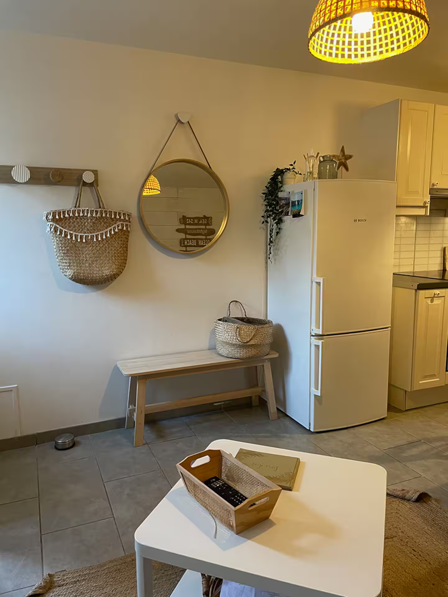 Un salon avec un réfrigérateur, une table, un banc et un miroir.