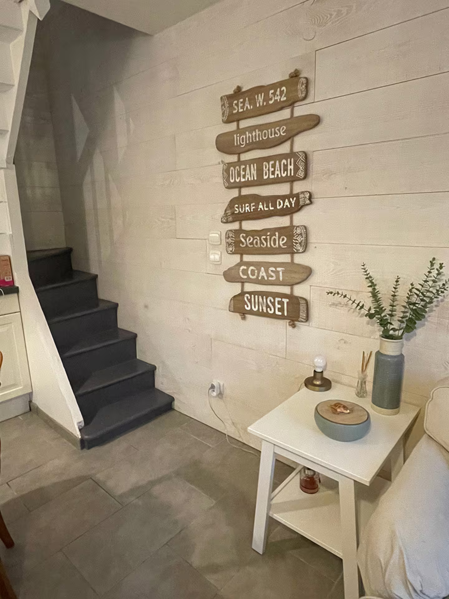 Un salon avec des escaliers, une table et un panneau sur le mur.