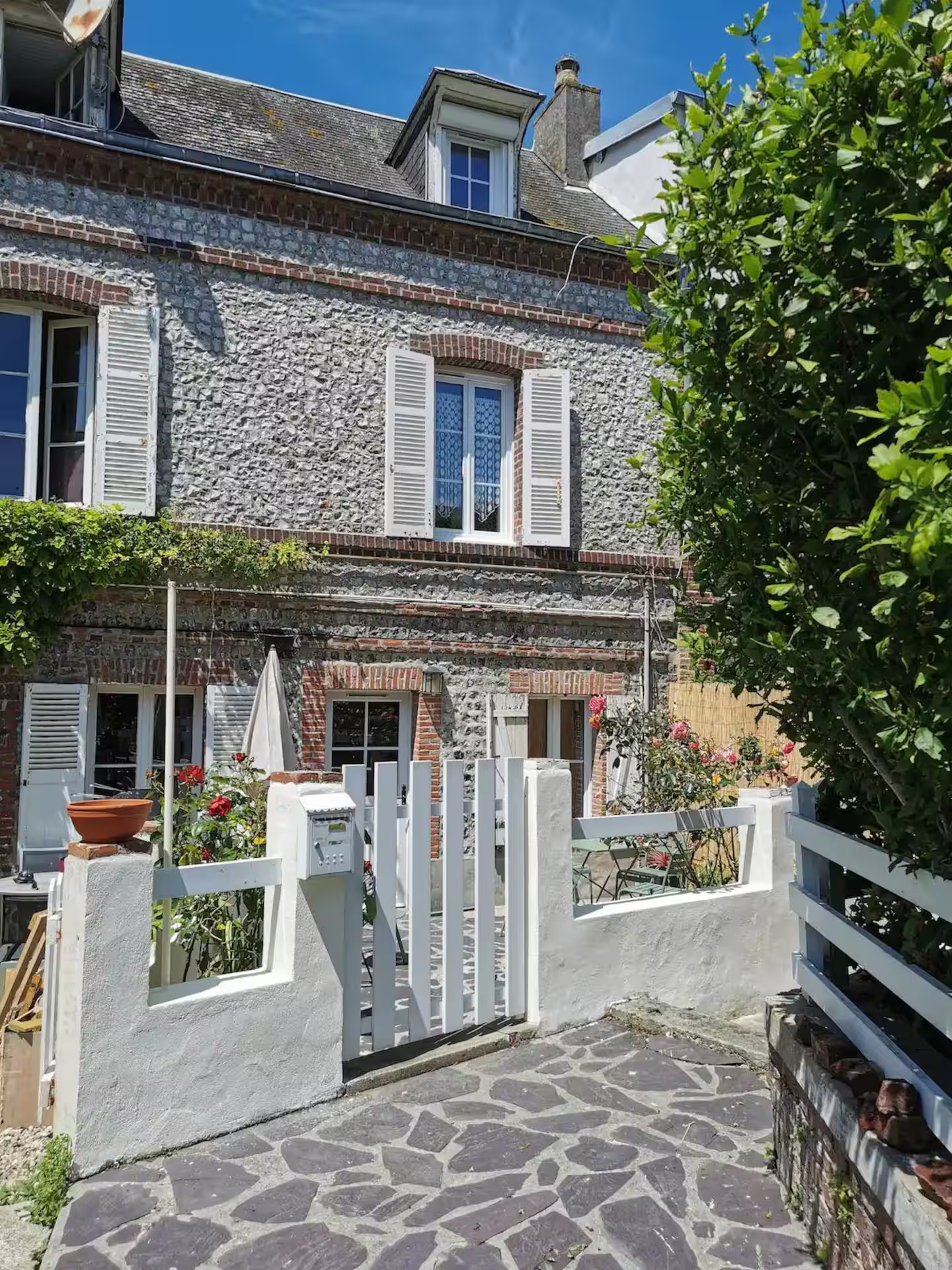 Une maison en pierre avec une clôture blanche et un portail blanc devant elle.
