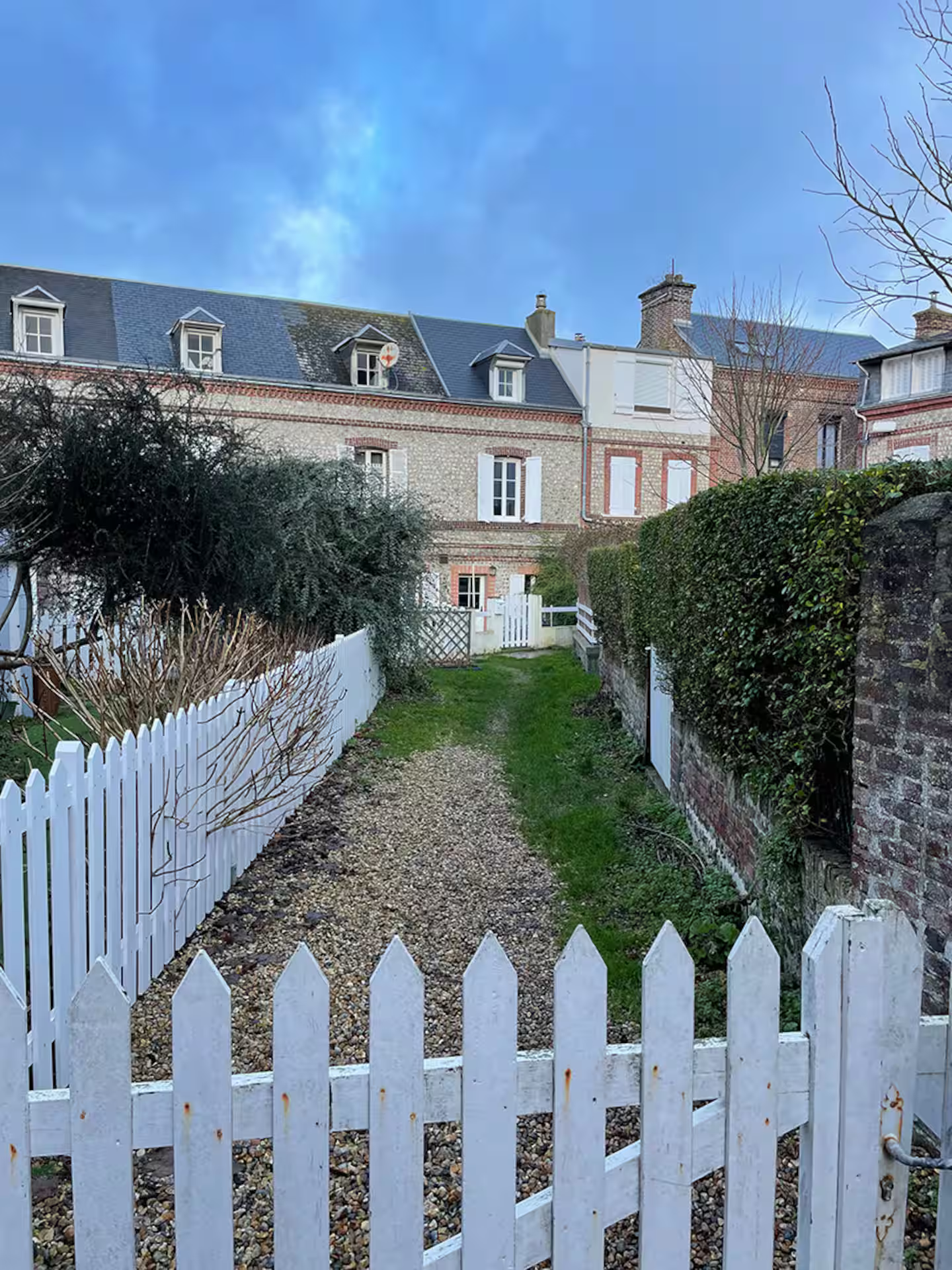 Une clôture blanche entoure un chemin de terre menant à une maison.