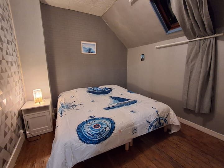 Chambre mansardée confortable avec un lit, une lampe de chevet et des murs gris sous un plafond mansardé.