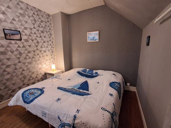Chambre avec un couvre-lit blanc, un imprimé nautique bleu, un mur d'accent gris et une petite lampe de chevet.
