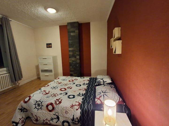 Chambre confortable avec un lit, une lampe de chevet, une commode blanche et un mur d'accent couleur rouille.