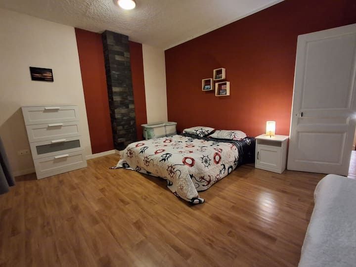Chambre confortable avec murs rouges, un lit, une commode blanche, une lampe de chevet et un parquet.