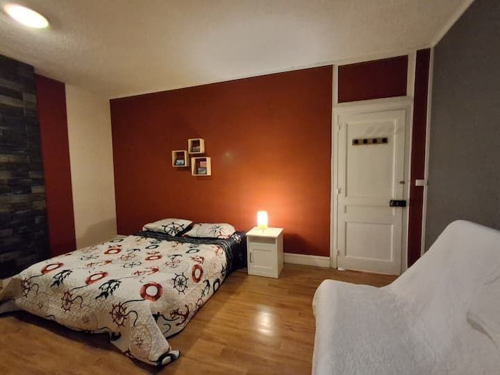 Chambre confortable avec un lit, une commode blanche, une lampe de chevet, un parquet et un mur d'accent rouge.