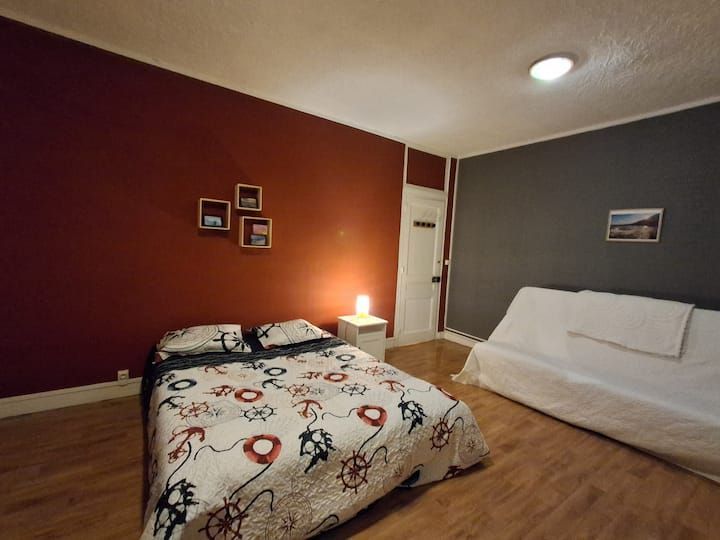 Chambre aux murs bordeaux, deux lits et une petite lampe de chevet sous un plafonnier.
