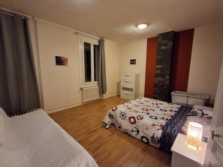 Petite chambre avec parquet, un lit, une commode, une fenêtre, des rideaux et une lampe de chevet.