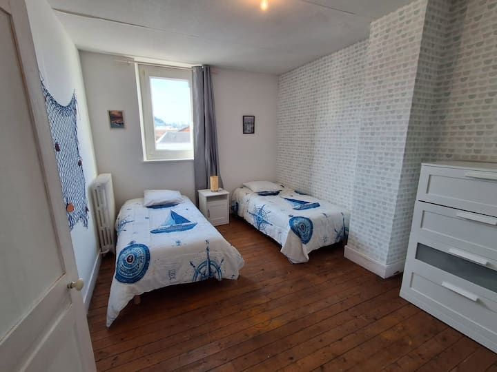 Petite chambre avec deux lits jumeaux, commodes blanches et linge de lit à motifs bleus et blancs.