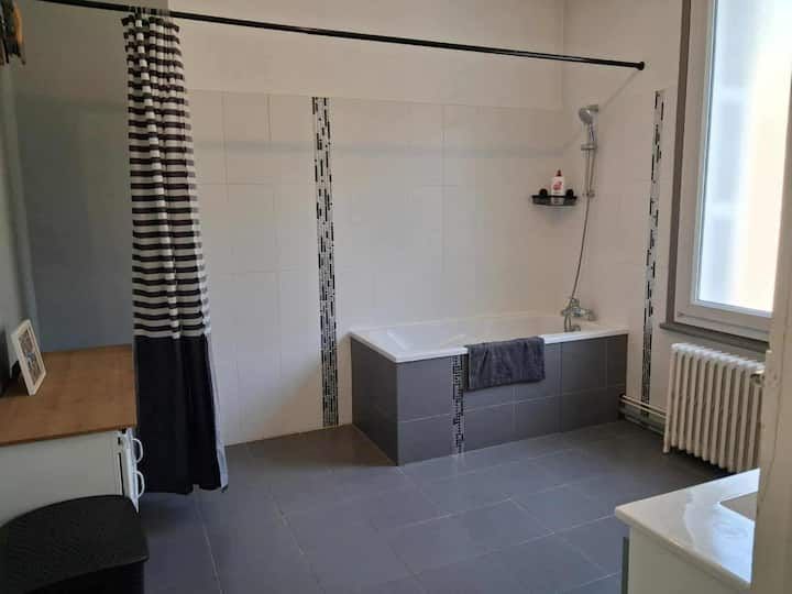 Chambre minimaliste avec rideau de douche, sol gris, radiateur et baignoire près d'une fenêtre
