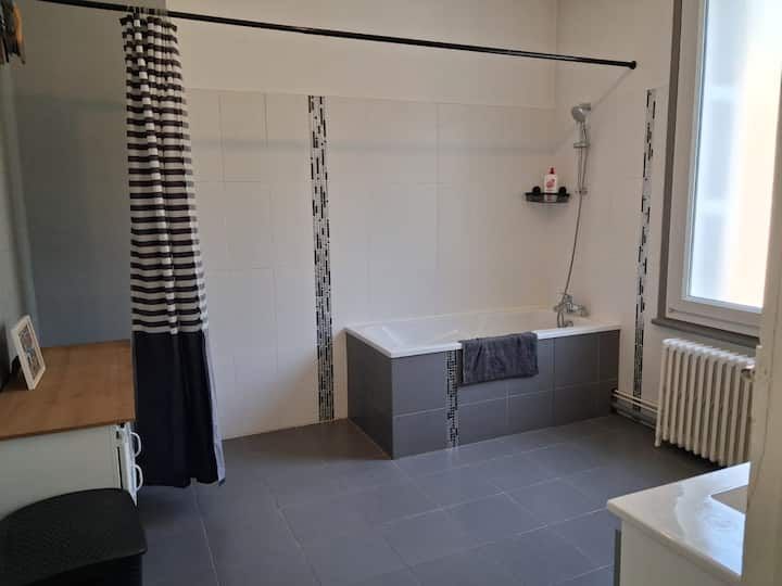 Pièce minimaliste avec sol carrelé gris, rideaux noirs et blancs, radiateur, fenêtre et banquette basse de rangement.