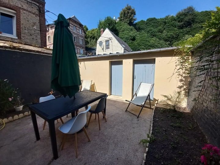 Cour ensoleillée avec table de patio noire, chaises, parasol, chaise longue et muret beige façon cabanon avec portes bleues