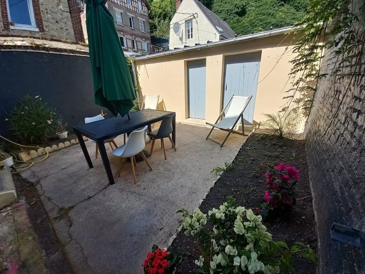 Terrasse avec table, chaises, parasol vert, transat et fleurs le long d'un mur beige