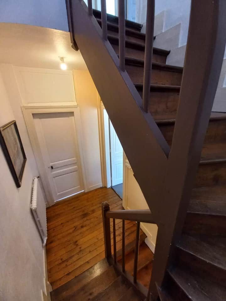 Escalier avec marches en bois, portes blanches et couloir clair vu du dessus.