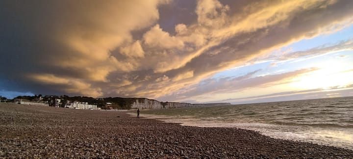 Plage de galets au coucher du soleil, avec des nuages et des vagues spectaculaires le long du rivage.